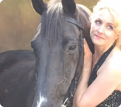 Iris Smalbeek with blonde hair, smiling softly, with the head of a dark horse positioned closely beside her